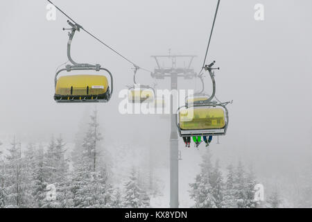 Ski chairlift bringing skiers and snowboarders up the Skrzyczne mountain after heavy snowfall on a misty winter day in Szczyrk ski resort in Poland Stock Photo