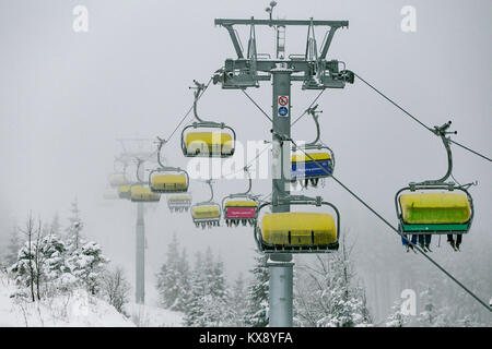 Ski chairlift bringing skiers and snowboarders up the Skrzyczne mountain after heavy snowfall on a misty winter day in Szczyrk ski resort in Poland Stock Photo