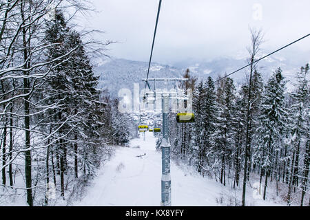 Ski chairlift bringing skiers and snowboarders up the Skrzyczne mountain after heavy snowfall on a misty winter day in Szczyrk ski resort in Poland Stock Photo