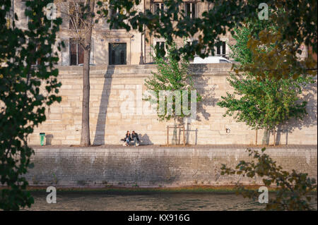 Young people Paris, view of a couple sitting together in sunshine along the Quai d'Orleans on the Ile St Louis in the centre of Paris, France. Stock Photo