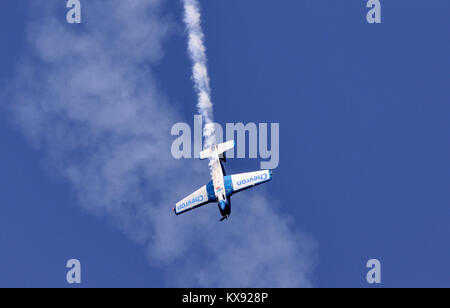 A small aerobatic aircraft performs a sharp dive during a flight display, trailing a thick plume of white smoke from its tail against a clear sky. Stock Photo