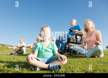 Child and group of people with disabled man practicing yoga. Stock Photo