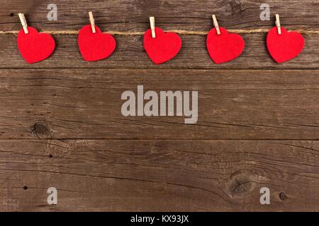 Cloth hearts hanging from line, top border against a rustic old wood background Stock Photo