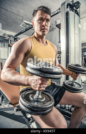 Man is sitting on a gintastic bench and is preparing to do exercises with dumbbell Stock Photo