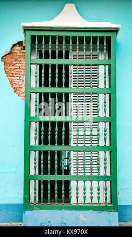 White shuttered window with green wooden bars on blue wall with cracks in Trinidad, Cuba Stock Photo