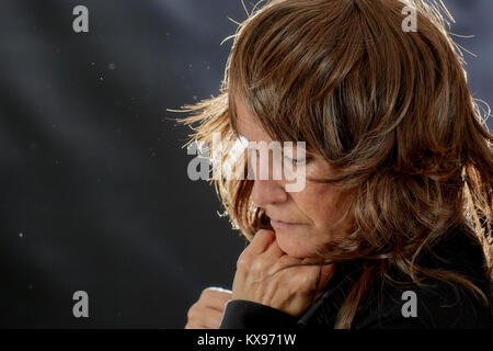 Middle aged woman appearing lonely and contemplative with chin on hands and layered brown hair and back lighting Stock Photo