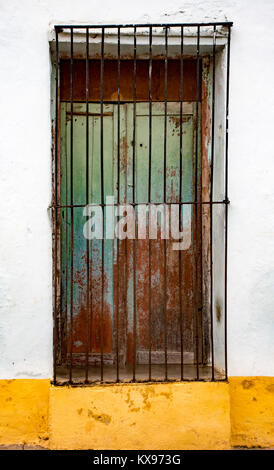 Green shuttered window with black iron bars on white and yellow wall, rusting in Trinidad, Cuba Stock Photo