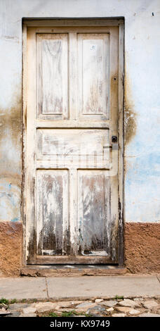 Cracking white painted door on blue stained wall in Trinidad, Cuba Stock Photo