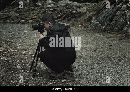 side view of passionate photographer who taking pictures with dslr and tripod at forest environment Stock Photo