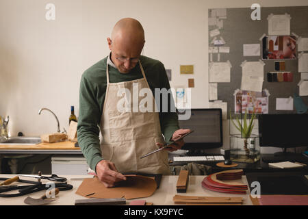 Male worker checking leather sheet while using digital tablet Stock Photo