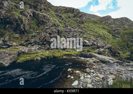 Stream flowing through the rocky green hills Stock Photo