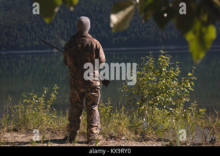 Hunter with shotgun standing near lake Stock Photo