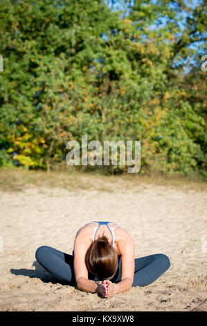 Woman practicing yoga in the sand - Bound Angle Pose Forward - Baddha Konasana - Autumn day Stock Photo