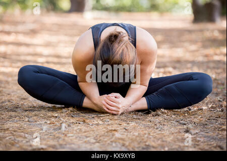 Woman practicing yoga in the sand - Bound Angle Pose Forward - Baddha Konasana - Autumn day Stock Photo