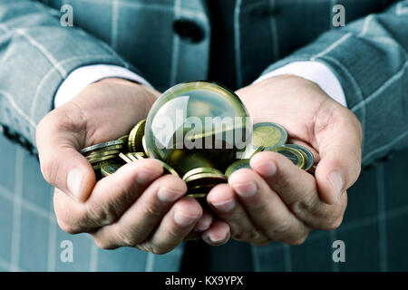 closeup of a young caucasian businessman wearing an elegant gray suit, with a pile of euro coins and a crystal ball in his hands Stock Photo