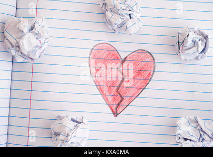 Broken Heart. Broken Heart on notebook sheet with some crumpled paper balls on it. Close up. Stock Photo