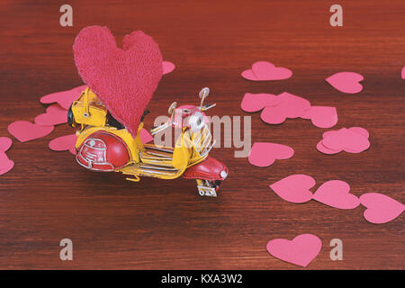 Vintage motorbike carry a red cushion heart on wooden background. Valentine's day. Delivery concept Stock Photo