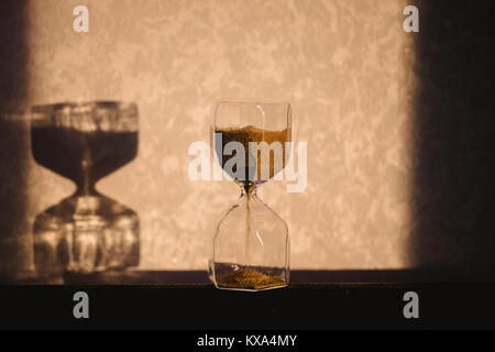 Hourglass with shadow on wall. Time passing concept for business deadline, urgency and running out of time. Sandglass, egg timer showing the last minu Stock Photo