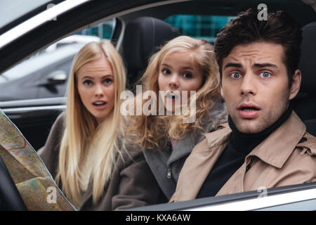 Image of shocked scared young man sitting in car with his wife and daughter. Looking camera holding map. Stock Photo