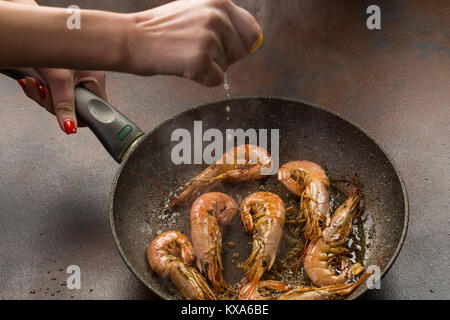 A hand squeezing lemon juice on roasted, grilled large tiger shrimps or langostonos over grey background. process of preparation Stock Photo