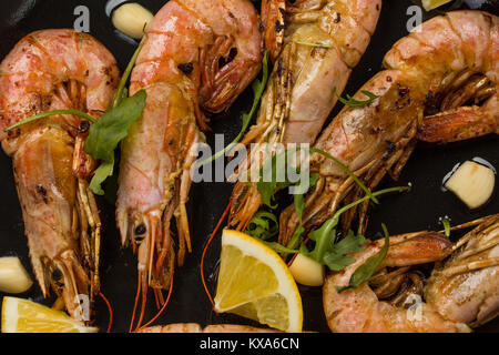 prawns shrimps with garlic, lemon, spices and italian parsley garnish in a black pan on white painted rustic wood, selected focus, narrow depth of fie Stock Photo