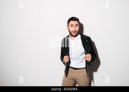 Portrait of a cheery young man in jacket posing while standing and looking at camera isolated over white background Stock Photo