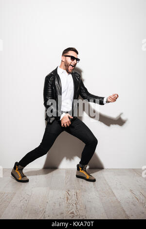 Full length portrait of an excited young man in sunglasses pretending playing on a guitar isolated over white background Stock Photo
