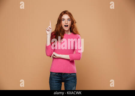 Portrait of an excited young redhead girl pointing finger up while having an idea isolated over beige background Stock Photo