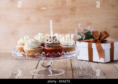 Delicious birthday cupcakes with one candle served on glass cakestand on festive wooden table Stock Photo