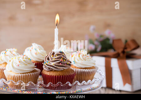 Delicious birthday cupcakes with one candle served on glass cakestand on festive wooden table Stock Photo