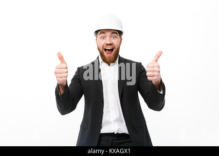 Cheerful bearded business man in protective helmet showing thumbs up and looking at the camera over white background Stock Photo