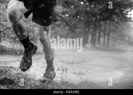 Low section of male runner splashing though puddle in Rancho Santa Elena, Hidalgo, Mexico Stock Photo