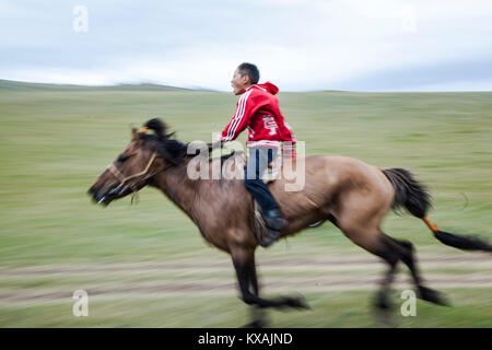 The horse races are by age five years with the riders no older than 13 years of age when they retire. Many of the riders wear vibrantly colored satin capes and matching suits to be recognized from a far distance. Most go bareback, though a few ride on light racing saddles. Many only wear socks to cut down on the weight of bulky boots and almost all have a dashur a crop to urge their horses on. They compete for 20 kilometers bareback horse race. Annual Naadam Festival in Bunkhan, Mongolia. Stock Photo