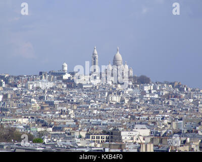 This image shows the Basilique du Sacré-Cœur in Paris, France, viewed from the Tour Montparnasse. The basilica, located on Montmartre Hill, is known for its distinctive white domes and is one of Paris's iconic landmarks. Stock Photo