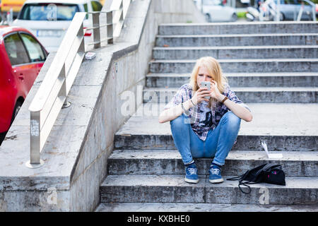 Young Caucasian woman using smart phone while sitting on stairs  Stock Photo