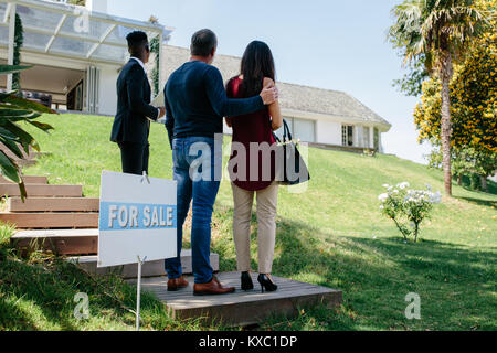 Rear view of couple visiting luxury villa with real estate agent. Property broker showing a house for sale to buyer couple. Stock Photo