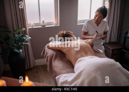 Female massage therapist talking to woman at wellness center and making notes. Beautician examining female client before spa treatment. Stock Photo