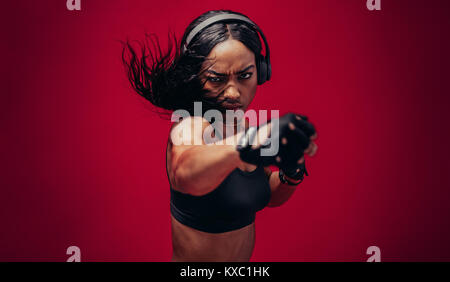 Boxer practicing her punches in a studio. African female boxer practicing boxing against red background. Stock Photo