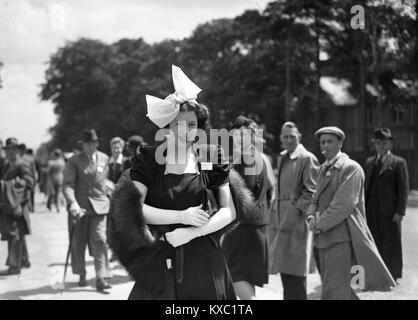 Heads turn to look at a fashionable young lady wearing her posh dress and hat at Royal Ascot 1937 Stock Photo