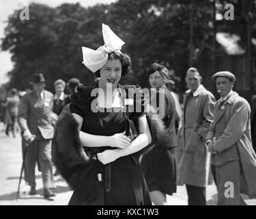 Heads turn to look at a fashionable young lady wearing her posh dress and hat at Royal Ascot 1937 Stock Photo