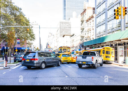 New York City, USA - October 27, 2017: Many cars, yellow taxi cabs, school buses, turning in traffic light with autumn trees, sidewalk, construction,  Stock Photo