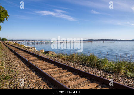 Railway line follows seafront, White Rock, BC, Canada. Wooden pier for pedestrians extends 1/2km (1650 feet) into Semiahmoo Bay off Strait of Georgia Stock Photo