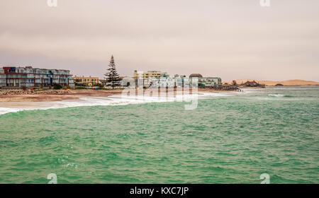 Waves, stones at the coastline with houses in background, Swakopmund German colonial town, Namibia Stock Photo