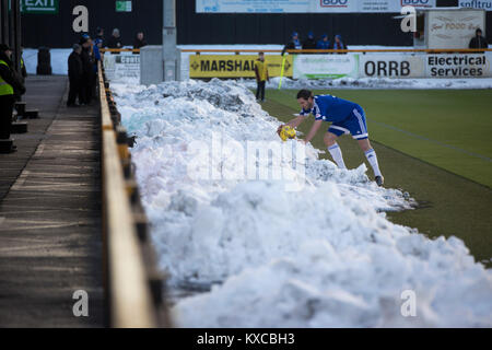 An away player retrieves the match ball from a pile of snow as Alloa Athletic take on Peterhead (in blue) in a Scottish League One fixture at Recreation Park, with the Ochil Hills in the background. The club was formed in 1878 as Clackmannan County, changing the name to Alloa Athletic in 1883. The visitors won the match by one goal to nil, watched by a crowd of 504.