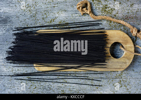 high angle view of a bunch of uncooked black spaghetti on a wooden chopping board, placed on a gray rustic wooden table Stock Photo