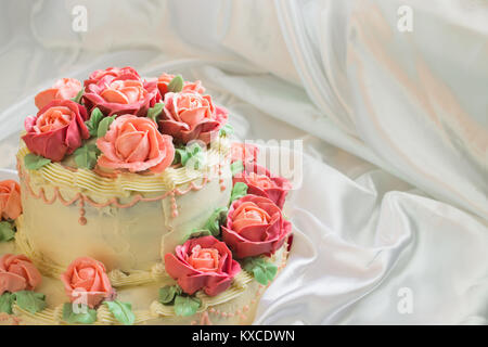 cream cake with roses closeup on a background of white satin fabric Stock Photo
