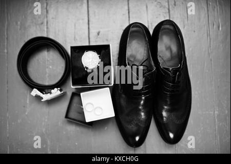 Close-up photo of black groom's brogue shoes, watch, wedding rings, belt and bow tie on the wooden background. Black and white photo. Stock Photo