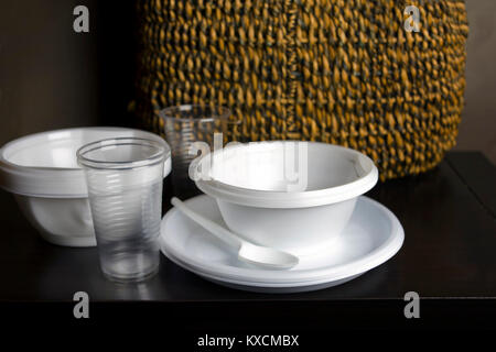 A bunch of plastic tableware placed on a table, a wicker basket in the background Stock Photo