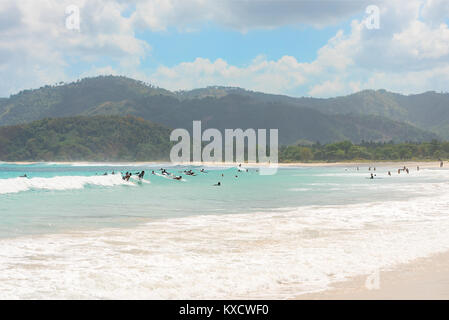 Large group of tourists learn to surf on small beginner waves at a paradise tropical beach, Kuta Lombok, Indonesia. Stock Photo