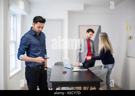businessman using smart phone with colleagues standing at desk in background Stock Photo